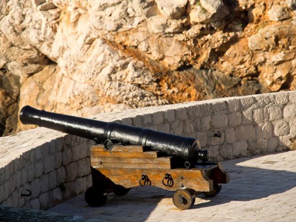 Black cannon on a wooden frame in front of a historic stone wall, the old town of Dubrovnik with