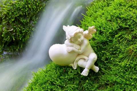 Porcelain angel figurine on moss by a waterfall