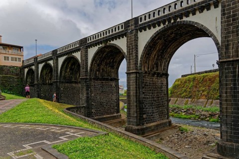 Historic eight-arched bridge over the Ribeira Grande River, surrounded by grasslands, under a