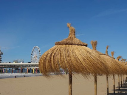 Beach with thatched parasols and a Ferris wheel in the background, parasols and a pier on the beach