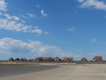A sandy beach in front of a settlement with red houses, under a blue sky with white clouds, Baltrum