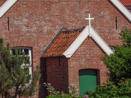 View of a brick church building with green painted door and white cross above, Baltrum Germany