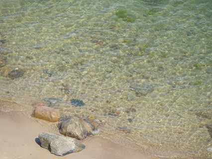 Clear water on the coastal shore with various stones on the sandy beach, spring on the Baltic Sea