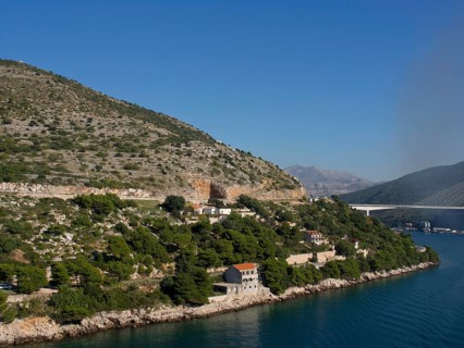 Coastal landscape with mountains, hills, bridges and houses on the shore of the calm blue sea under