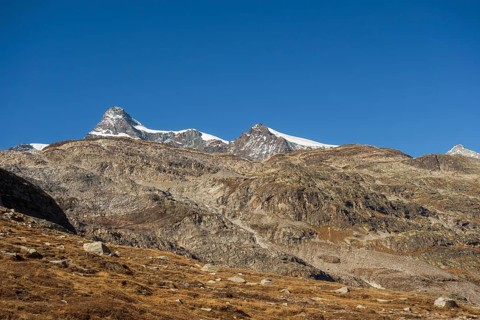 Striking peaks above rocky landscape and sparse snow under clear blue sky, bare mountain peaks with