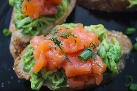 Gourmet avocado toast topped with smoked salmon, garnished with fresh dill and green onions on a