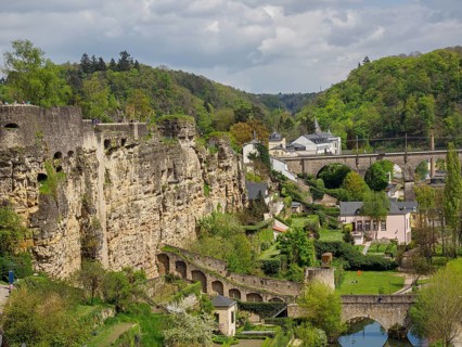 Rocky cliff landscape with a bridge, buildings and lush greenery around a river, overlooking a