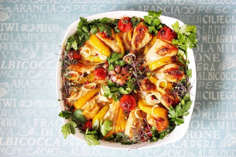 Roasted chicken and bell peppers arranged in a white dish with cherry tomatoes and parsley on a