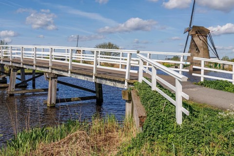 White bridge over a canal, windmill in the background, calm nature-related atmosphere, windmills of