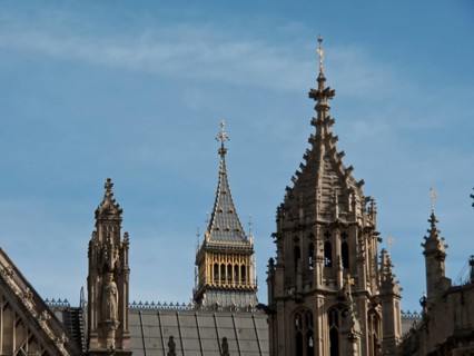 Detail of a gothic building with towers and roof spires, smaller tower in the background, blue sky,