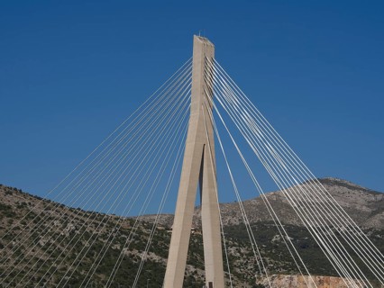 Modern suspension bridge with ropes in front of a clear blue sky and mountains, the old town of