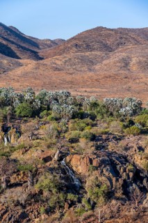 Kunene River with green vegetation in dry red mountain landscape, waterfall and African Baobab
