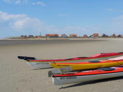 Several kayaks on the beach with a view of a coastal landscape and traditional houses, Baltrum