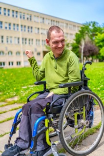 Vertical exterior portrait of a disabled man smiling sitting in the electric wheelchair in the