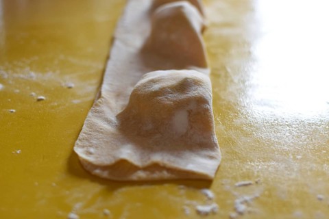 Preparation of fresh homemade pasta mezzaluna with ricotta, folded dough in front of cutting out