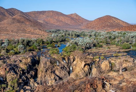 Kunene River with green vegetation in dry red mountain landscape, waterfall and African Baobab