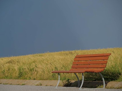 Lonely wooden bench on a grassy field under a dark, cloudy sky, Baltrum Germany