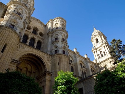 Imposing cathedral with two towers and richly decorated facades against a blue sky, Malaga on the