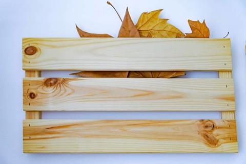 Dried tree leaves hanging on a wooden hanger on a blue wall