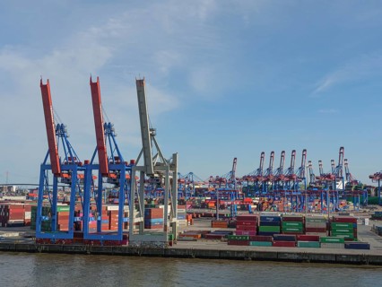 An industrial harbour terminal with lots of containers, cranes and storage areas on a sunny day, a