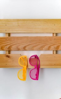 Funny colorful plastic glasses hanging on a wooden shelf on a white wall