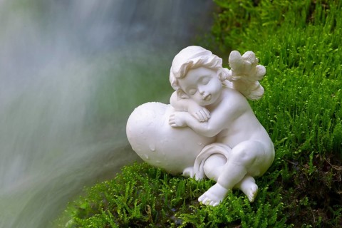 Porcelain angel figurine on moss by a waterfall