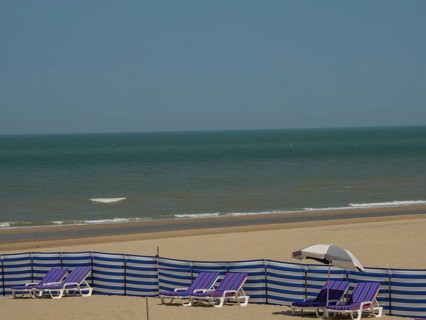 A peaceful beach with blue striped deckchairs, a parasol and the calm sea in the background,
