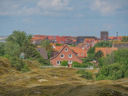 A village with red roofs, nestled between green hills and trees, Baltrum Germany