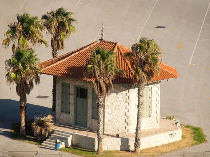 Small pavilion with red roof tiles surrounded by palm trees on an asphalted area, Ancient building