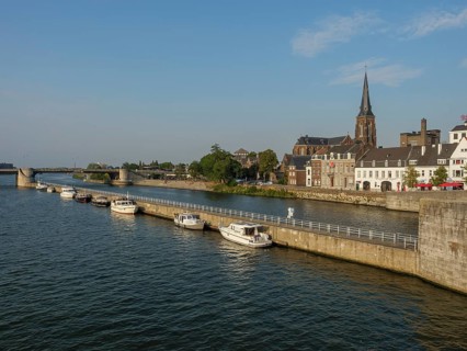 River view with neighbouring boats, historic buildings and a church, a bridge in the distance,