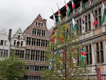 Historic buildings with ornate gables and many flags, trees in front under a gloomy sky, Historic