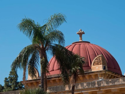 Historic building with red dome behind palm trees in front of a bright blue sky, palermo in sicily