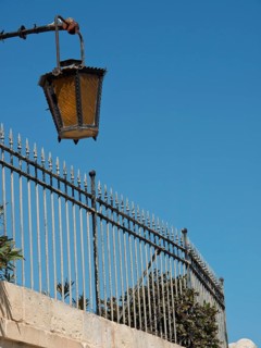 Street lamp over a metal fence with blue sky in the background, the town of mdina on the island of