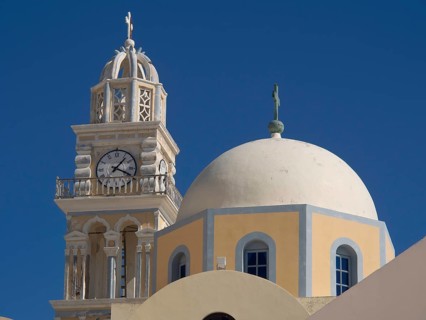 A tall bell tower and a domed church rise up against a bright blue sky, The volcanic island of