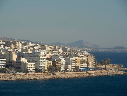 Several residential buildings along a rocky coast, with mountains in the background and a view of
