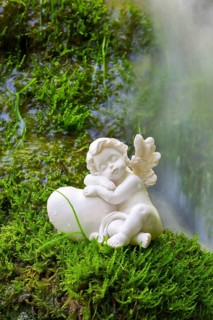 Porcelain angel figurine on moss by a waterfall