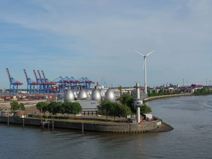 Harbour view with wind power plant, spherical tanks, containers and green trees under a clear sky,
