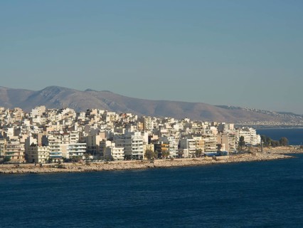 Coastal city skyline with many buildings bordering the blue sea and mountains in the background