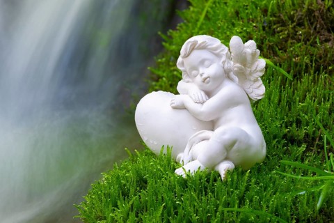Porcelain angel figurine on moss by a waterfall