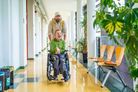 Male friend helping a man with disability in wheelchair to move around the university