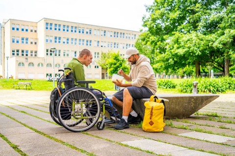 University student helping and eating with a disabled friend in the campus