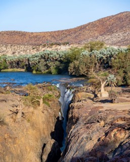 Kunene River with green vegetation in dry red mountain landscape, waterfall and African Baobab