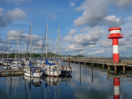 Clear harbour view with sailing boats and a red and white lighthouse under blue sky and scattered