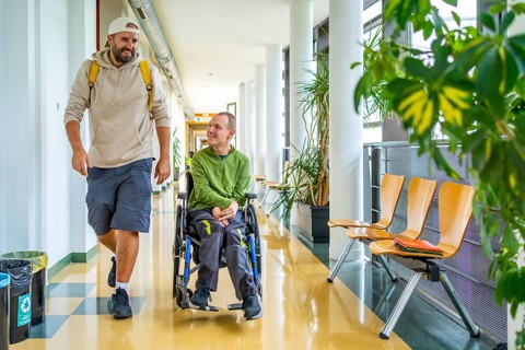 Man with physical disability in wheelchair and friend chatting distracted in the university
