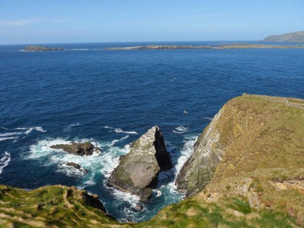 Impressive cliff landscape with rough waves crashing against rocks, under a blue sky, green meadows