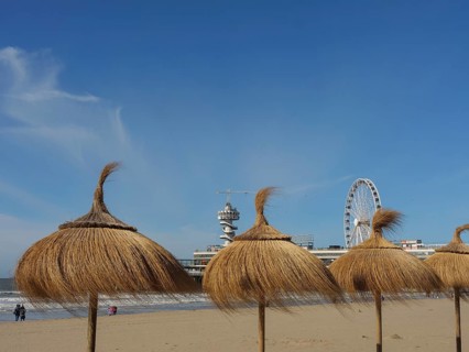 Beach with thatched huts and Ferris wheel under a clear sky, parasols and a pier on the beach of