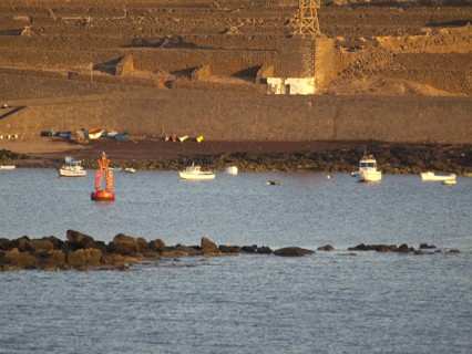 Boats and buoys on the sea in front of a rocky coastline at sunset, Lanzarote with a hisotric