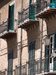 Buildings with green shutters and iron balconies, lanterns on the facade, shadow play on the wall,