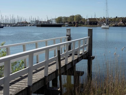 A wooden jetty leads into a lake, boats are moored on the shore, the surroundings appear calm and