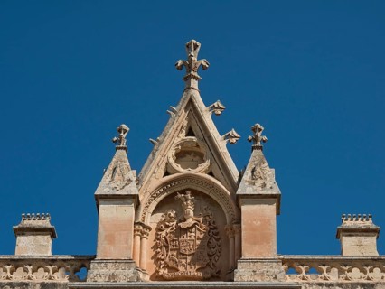 Detailed pediment with ornate coat of arms and elegantly designed spires under a clear blue sky,